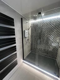 Bathroom with dark tiles and strip lighting around shower